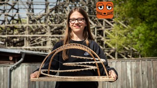 Ein Mädchen mit Brille hält ein selbstgebautes Modell von einer Achterbahn in den Händen