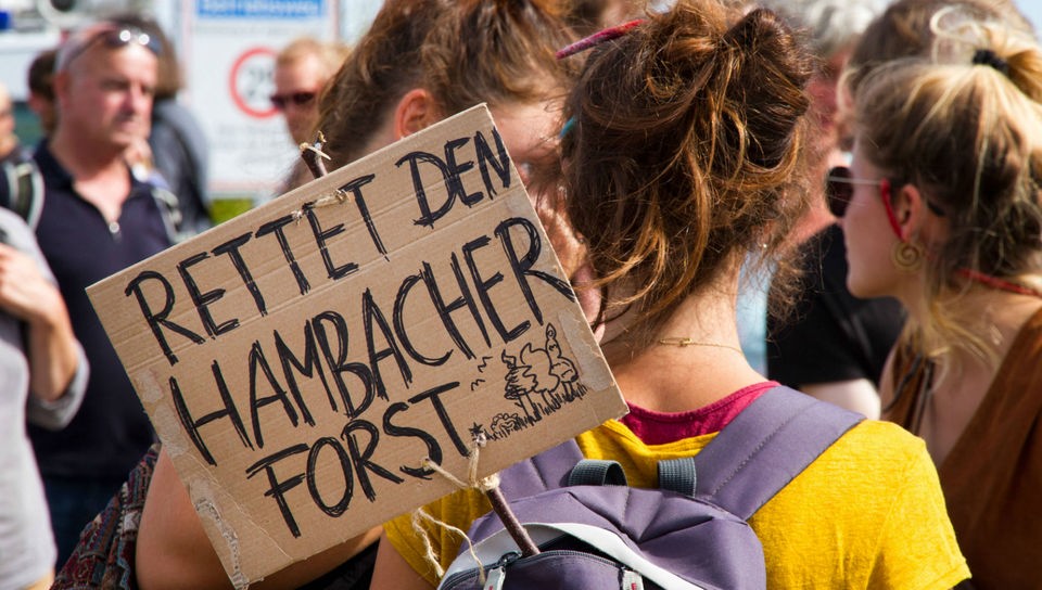 Plakat hängt auf dem Rücken eines Mädchens. Aufschrift: Rettet den Hambacher Forst.