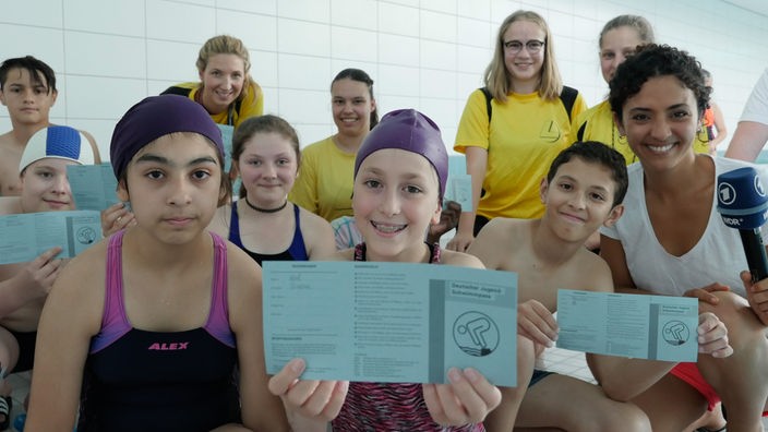 Siham gemeinsam mit den Schülern der Schwimm-AG des Leibniz-Gymnasiums Essen. Einige der Schüler halten ihren Jugend-Schwimmpass in die Kamera.