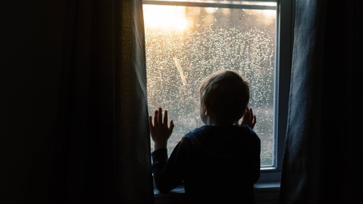 Kind schaut aus dem Fenster den Sonnenuntergang an