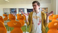 Robert in leerem Klassenzimmer mit orangen Stühlen