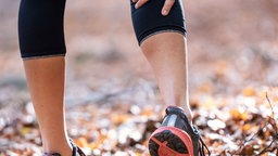 Auf dem Bild ist eine Person beim Joggen im herbstlichen Wald zu sehen, die sich wegen eines Krampfes an das Bein fasst.