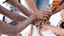 Eine Gruppe von Menschen mit unterschiedlichen Hautfarben legt die Hände übereinander.