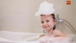 Ein Mädchen sitzt mit Schaum auf dem Kopf in einer Badewanne