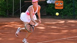 Eine Frau hält einen Tennisschläger in der Hand und versucht an einen gelben Tennisball zu kommen.