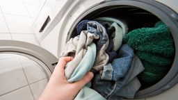 Eine Frauenhand stopft Wäsche in die Waschmaschine