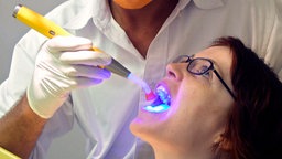 Zahnarzt leuchtet mit blauem Licht in den Mund einer Patientin