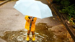 Kind mit Regenschirm in einer Pfütze