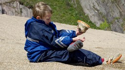 Ein Junge schüttelt Steine aus seinem Schuh