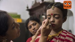 Frau malt Indischem Kind einen roten Punkt, Bindi genannt, auf die Stirn