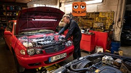 Ein Automechaniker arbeitet am Motor eines roten Autos in einer Werkstatt.