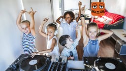 Kinder feiern eine Party und stehen an einem DJ-Pult 