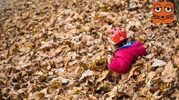 Ein kleines Mädchen spielt in einem großen Haufen Herbstlaub