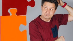 Moderator André neben zwei zusammengesteckten Puzzleteilen, die nicht zusammenpassen
