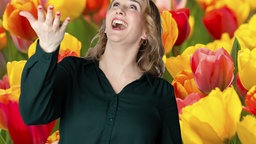 Fotomontage: Mausmoderatorin Marie vor einem bunten Tulpenfeld