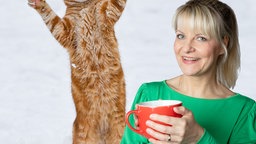 Fotomontage: Maus-Moderatorin Nina hält eine rote Tasse in der Hand, im Hintergrund steht eine Katze auf den Hinterpfoten im Schnee