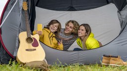 Drei Geschwister sitzen in einem Zelt und machen ein Selfie.