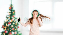 Mädchen tanzt mit Kopfhörern vorm Weihnachtsbaum