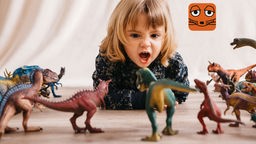 Ein Kind liegt auf dem Boden und schreit Plastik-Dinosaurier an.
