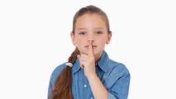Ein Mädchen legt den Zeigefinger auf seine Lippen