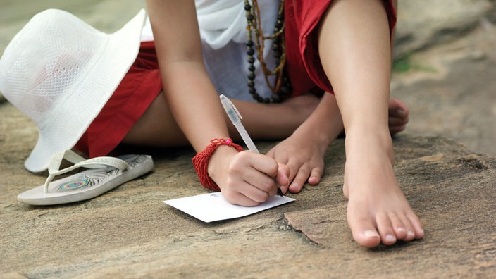 Ein Mädchen schreibt eine Postkarte auf dem Boden