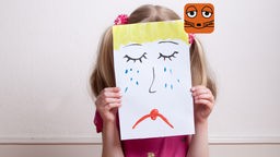 Ein Mädchen hält ein Bild von einem weinenden Gesicht hoch