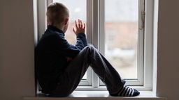Ein trauriges Kind schaut aus einem Fenster
