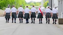 Eine Männergruppe trägt karierte Schottenröcke.