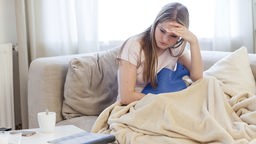 Eine junge Frau liegt mit Bauchschmerzen im Bett.