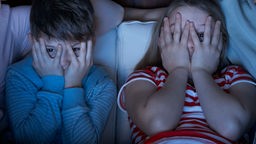 Zwei Kinder halten sich die Hände vor die Augen beim Fernsehen