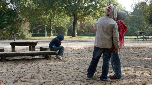 Zwei Kinder zeigen auf einem Spielplatz mit dem Finger auf ein anderes Kind