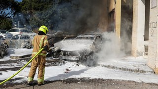 Feuerwehrman in Israel versucht nach einem Angriff der Hamas das Feuer auf Autos zu löschen
