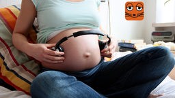 Eine schwangere Frau hält Kopfhörer auf ihren Bauch