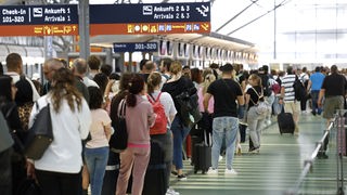 Passagiere stehen in einer Schlange von mehreren hundert Metern für die Sicherheitskontrolle am Flughafen Köln-Bonn an.