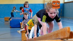 Eine Gruppe sechs Kindern klettert in einer Turnhalle über Kästen und Leitern.