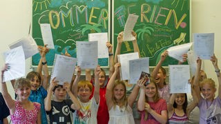Kinder einer 5. Klasse halten ihre Zeugnisse hoch und freuen sich auf die Sommerferien