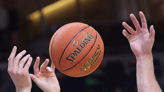 Ein Basketball, drei Hände, die sich danach strecken