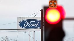 Das Logo des Autobauers Ford an seinem Standort in Köln neben roter Ampel