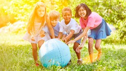 Vier Kinder unterschiedlicher Herkunft spielen mit einer Weltkugel
