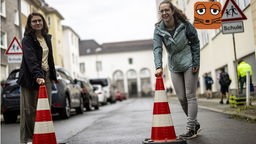 Eine Mutter stellt Pylonen auf, um eine Straße vor einer Schule zeitweise zu sperren.