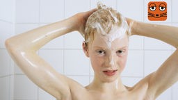 Ein rothaariger Junge wäscht sich unter der Dusche die Haare.