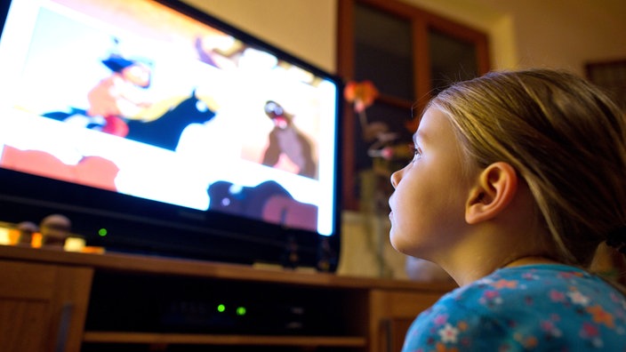 Mädchen sitzt nah vor einem Fernseher und schaut einen Comicfilm