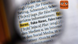 Durch eine Lupe ist der Text: Fake News im Duden zu sehen
