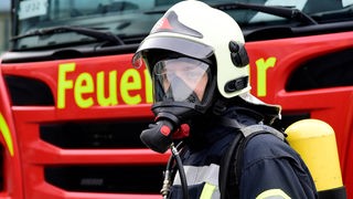 Feuerwehrmann mit Atemschutzmaske vor einem Feuerwehrlöschwagen
