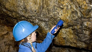 Mädchen erforscht Höhlenwand mit Taschenlampe