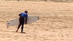 Das Surfcamp - Surfer legt sein Brett am Strand in den Sand
