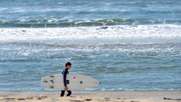 Das Surfcamp - Surfer trägt sein Brett am Strand
