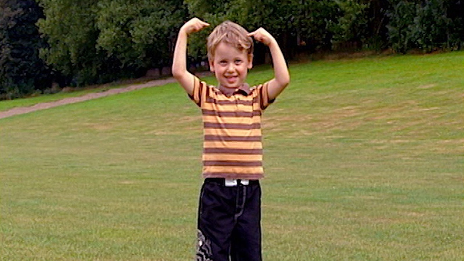 Eine Junge steht im Park und hebt die Arme hoch