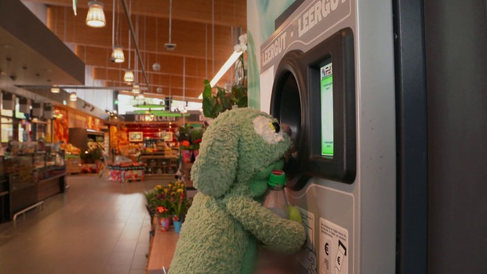 Stofftier Knolle vor einem Pfandflaschenautomaten