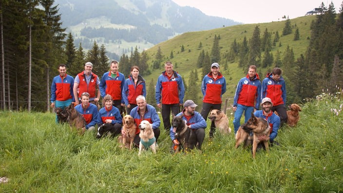 Das Team und ihre Lawinenhunde auf einer Bergwiese